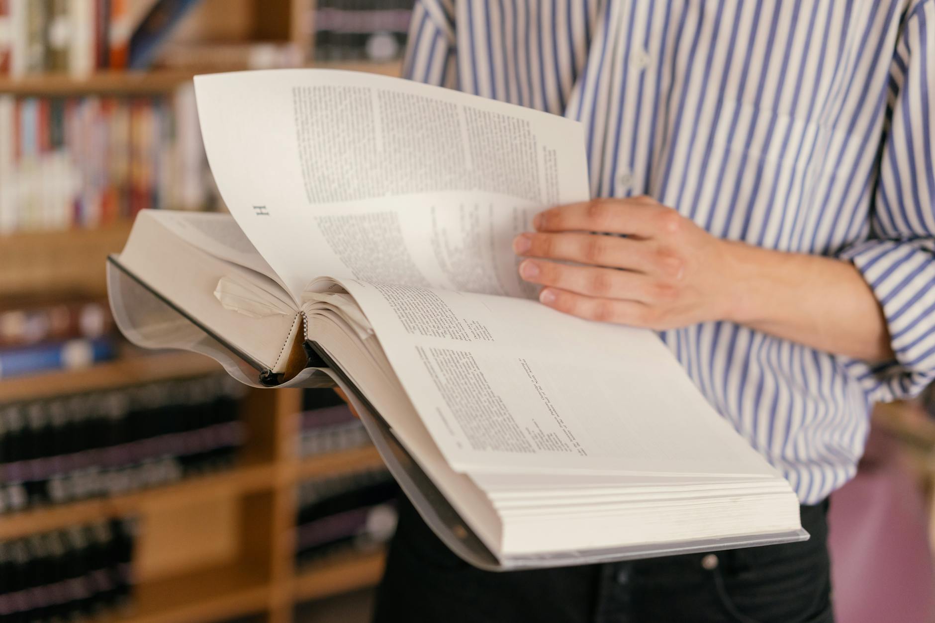 Osoba czytająca dużą otwartą książkę w bibliotece