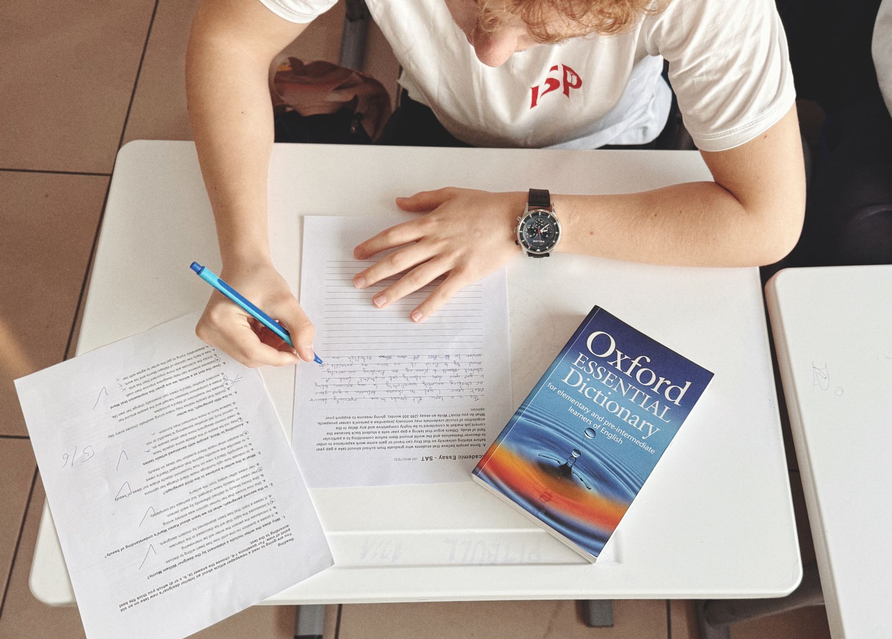 Uczeń pisze test po angielsku przy biurku z papierem i słownikiem Oxford
