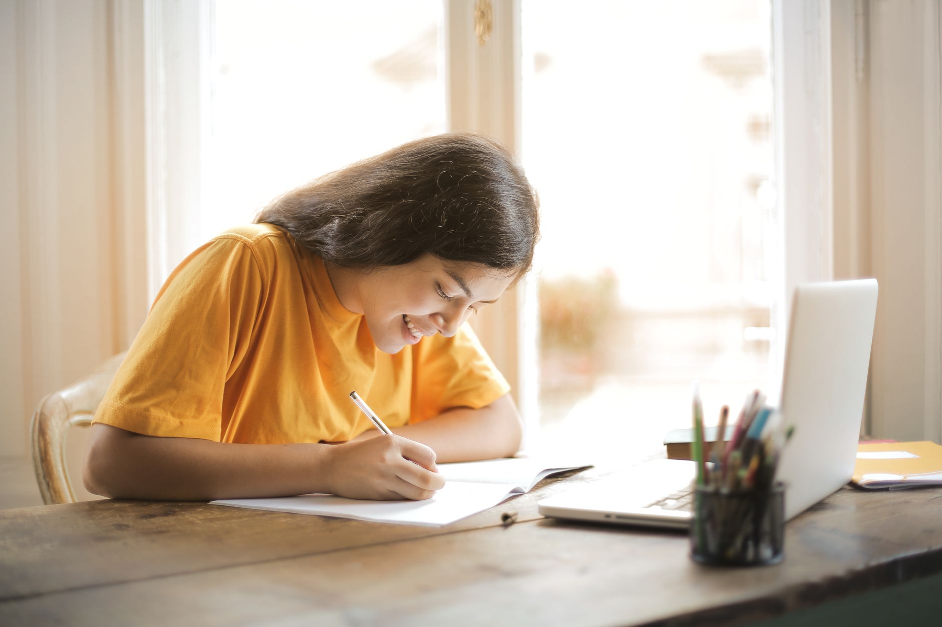 Studentka uczy się przy laptopie i notatniku w domu, uśmiechnięta